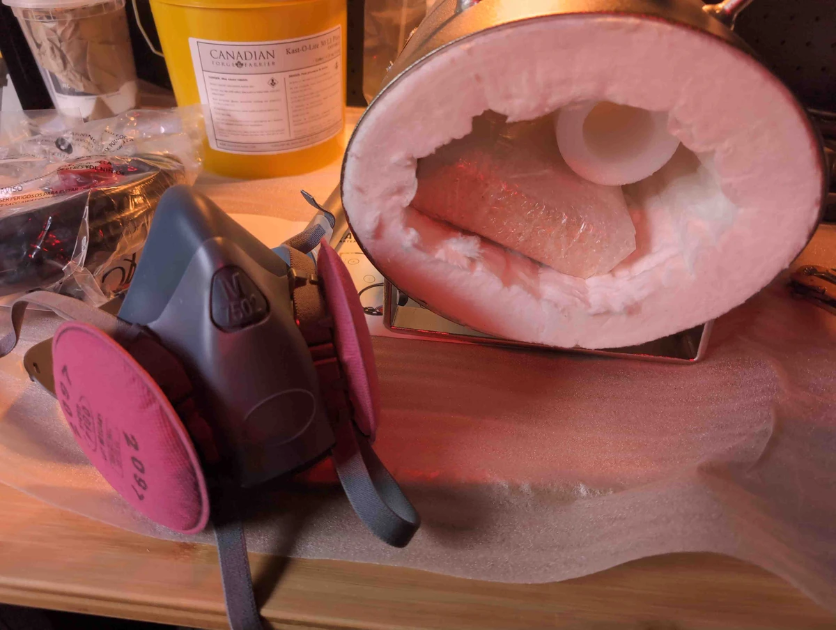 A half-face respirator next to a propane forge with unsealed ceramic wool blanket.