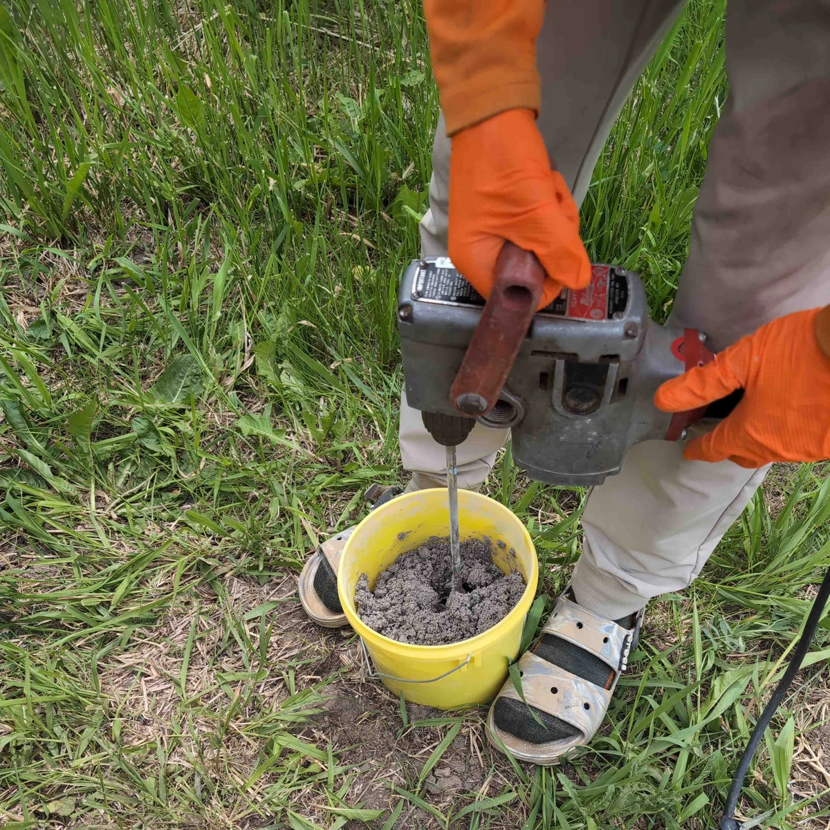 A heavy duty drill mixing refractory cement in a bucket.